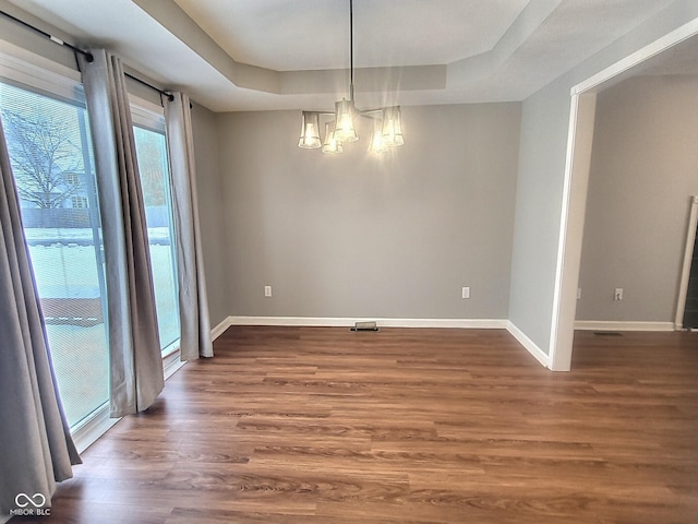 unfurnished dining area featuring dark hardwood / wood-style floors, an inviting chandelier, and a tray ceiling