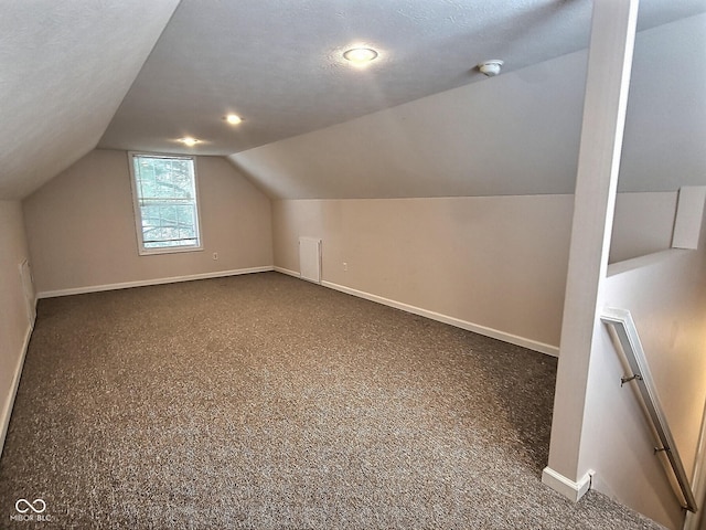 additional living space featuring lofted ceiling, a textured ceiling, and dark colored carpet