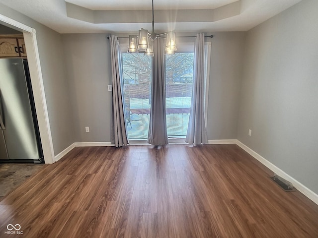 unfurnished dining area featuring a tray ceiling, dark hardwood / wood-style flooring, and a notable chandelier