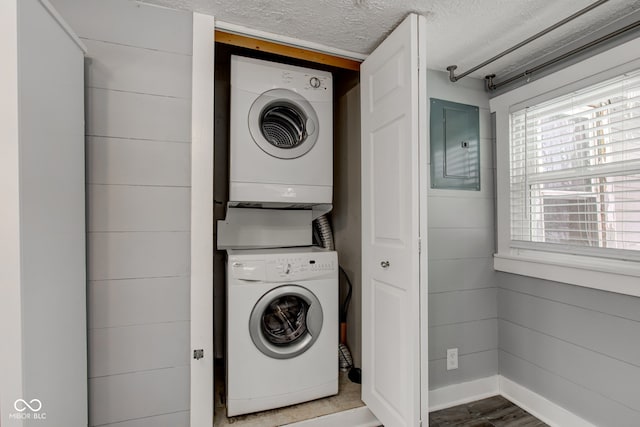 washroom with wood-type flooring, electric panel, wooden walls, a textured ceiling, and stacked washer and dryer