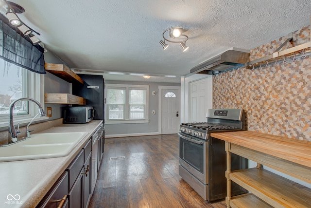 kitchen with a textured ceiling, dark hardwood / wood-style floors, stainless steel appliances, wall chimney range hood, and sink