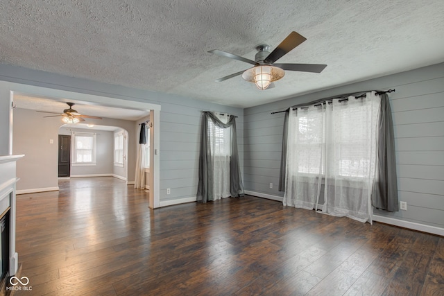 unfurnished living room featuring a textured ceiling, wood walls, ceiling fan, and dark hardwood / wood-style flooring