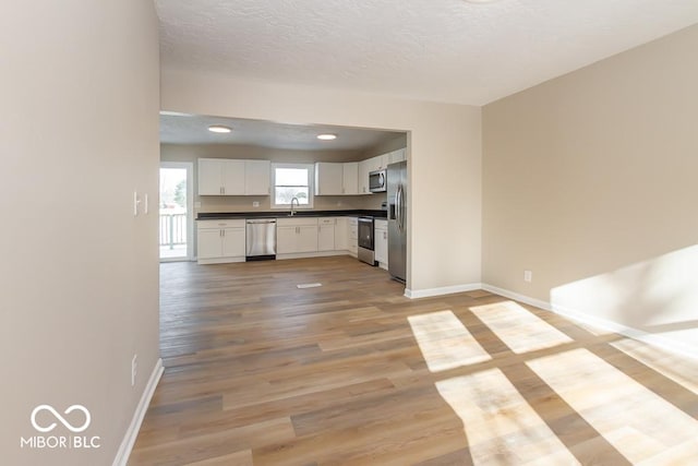 kitchen with sink, a textured ceiling, light hardwood / wood-style floors, white cabinetry, and stainless steel appliances