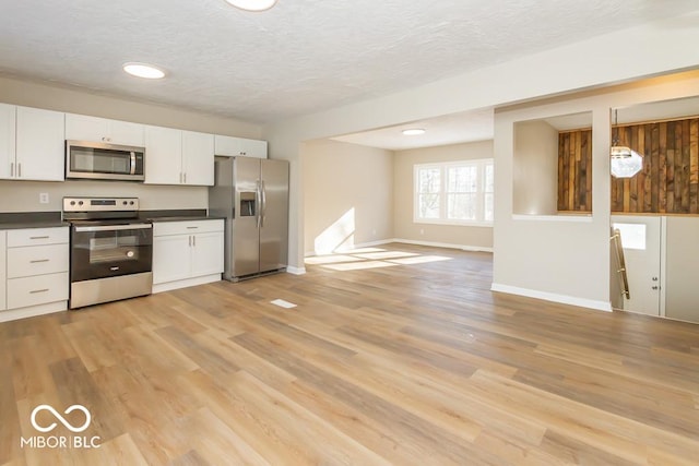 kitchen with white cabinets, appliances with stainless steel finishes, light wood-type flooring, and hanging light fixtures