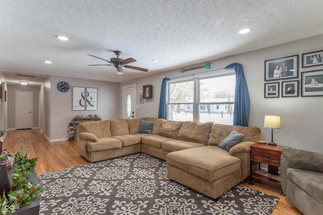 living room featuring ceiling fan, light wood-type flooring, and a textured ceiling