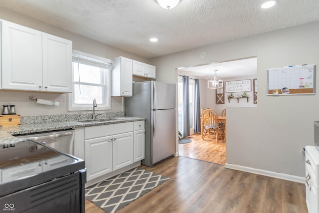 kitchen with white cabinets, sink, hanging light fixtures, a textured ceiling, and stainless steel appliances