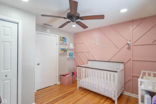 bedroom with a nursery area, a closet, light hardwood / wood-style flooring, and ceiling fan