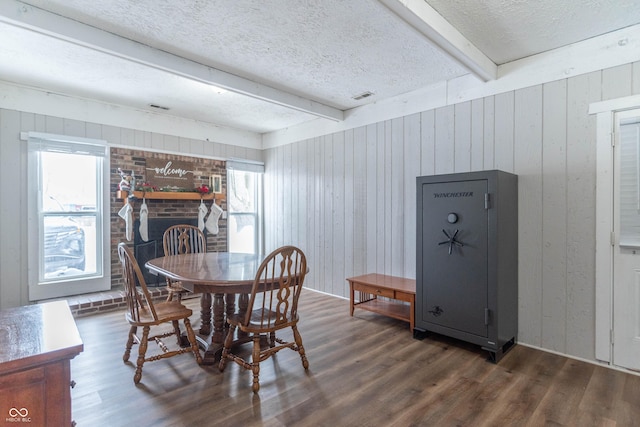 dining room featuring wood walls, a brick fireplace, dark hardwood / wood-style floors, a textured ceiling, and beamed ceiling