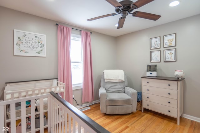 bedroom featuring light hardwood / wood-style flooring, a nursery area, and ceiling fan