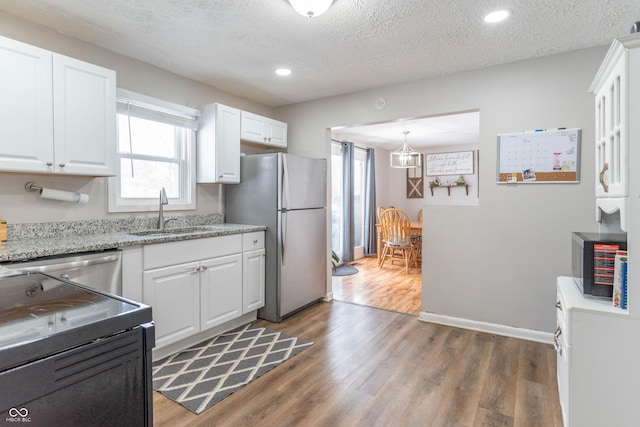 kitchen with appliances with stainless steel finishes, a textured ceiling, sink, pendant lighting, and white cabinetry