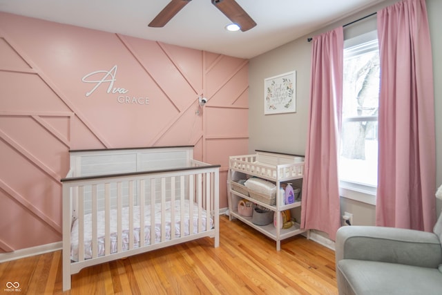 bedroom featuring ceiling fan, hardwood / wood-style floors, and a crib