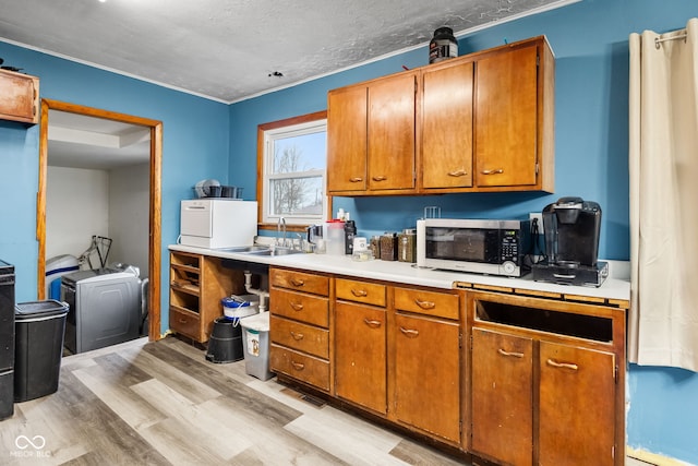 kitchen with a textured ceiling, washing machine and dryer, light wood-type flooring, and sink