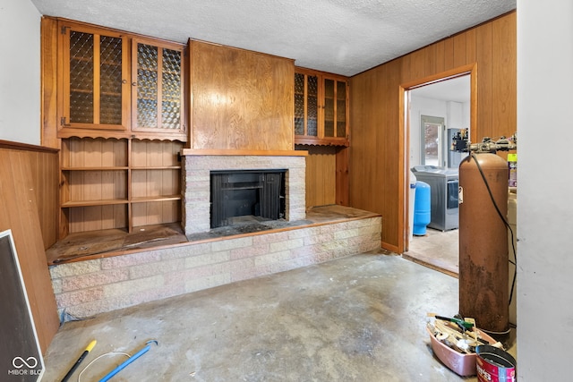 unfurnished living room with concrete flooring, a textured ceiling, washer and clothes dryer, a fireplace, and wood walls