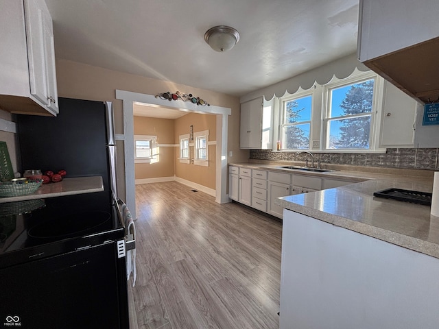 kitchen with black / electric stove, decorative backsplash, light wood-type flooring, white cabinetry, and sink