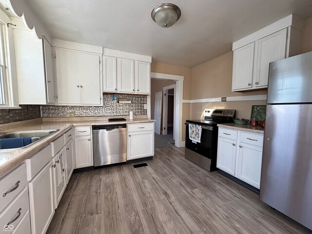 kitchen featuring appliances with stainless steel finishes, light hardwood / wood-style flooring, white cabinetry, and backsplash