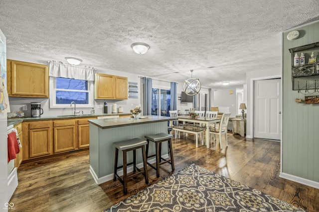 kitchen with a breakfast bar, sink, decorative light fixtures, a kitchen island, and dark hardwood / wood-style flooring