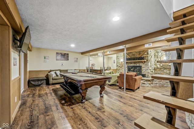 rec room featuring a stone fireplace, billiards, wood walls, hardwood / wood-style floors, and a textured ceiling