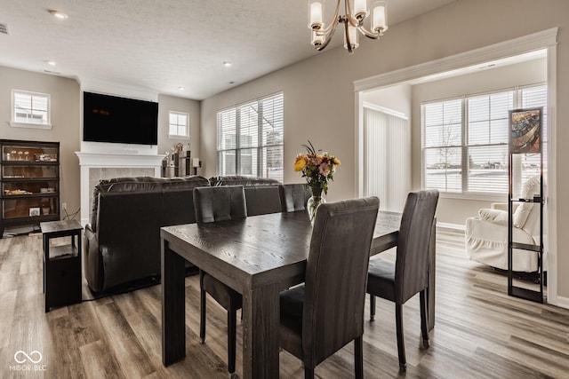 dining area featuring a tiled fireplace, a textured ceiling, hardwood / wood-style flooring, and a notable chandelier