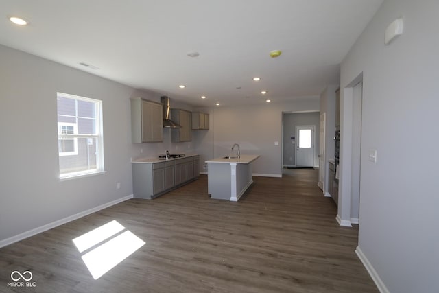 kitchen with baseboards, visible vents, an island with sink, gray cabinetry, and wall chimney exhaust hood