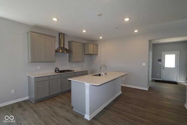 kitchen featuring dark wood-style floors, a kitchen island with sink, gray cabinets, a sink, and wall chimney range hood