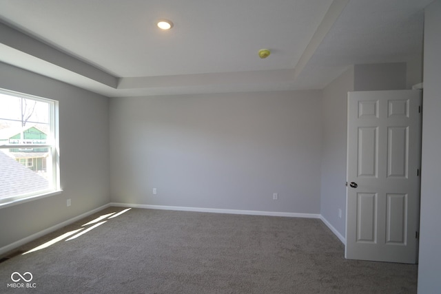 carpeted spare room with a tray ceiling and baseboards