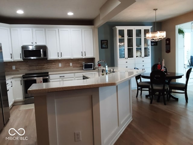 kitchen featuring pendant lighting, tasteful backsplash, a kitchen island with sink, white cabinetry, and appliances with stainless steel finishes