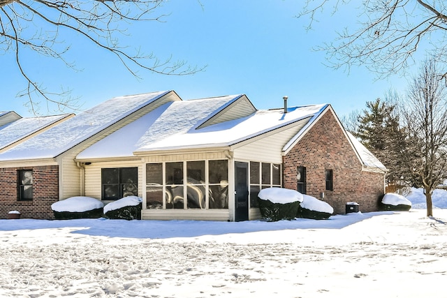 snow covered rear of property featuring a sunroom