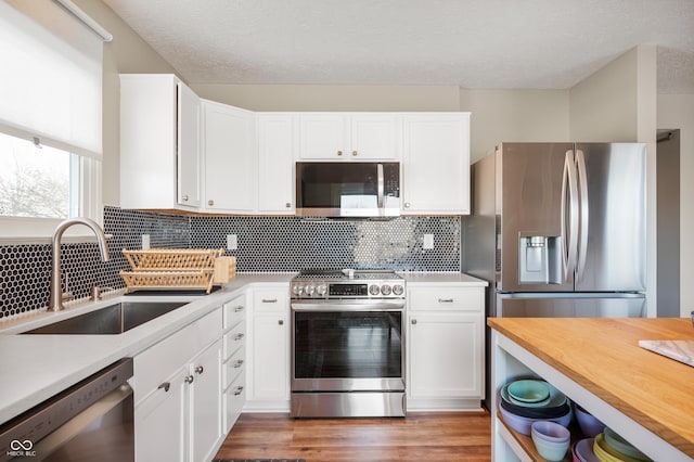 kitchen with hardwood / wood-style floors, tasteful backsplash, sink, white cabinets, and stainless steel appliances