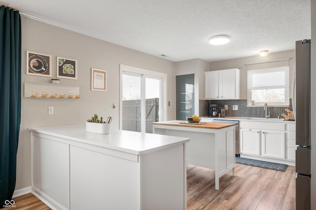 kitchen with a textured ceiling, decorative backsplash, white cabinets, a kitchen island, and stainless steel appliances