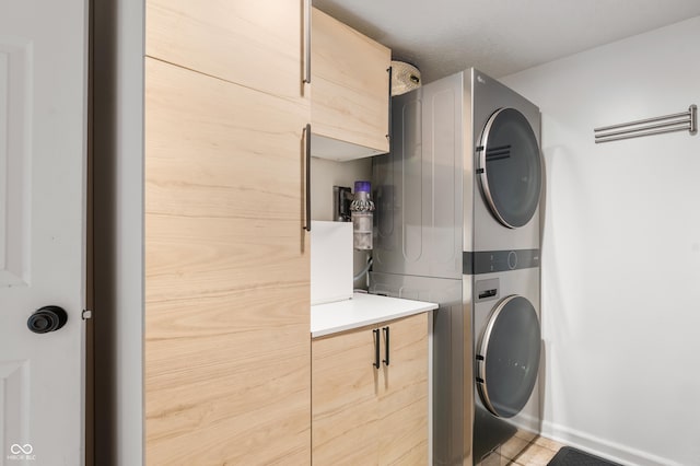 laundry room with stacked washer / dryer, cabinets, and tile patterned floors