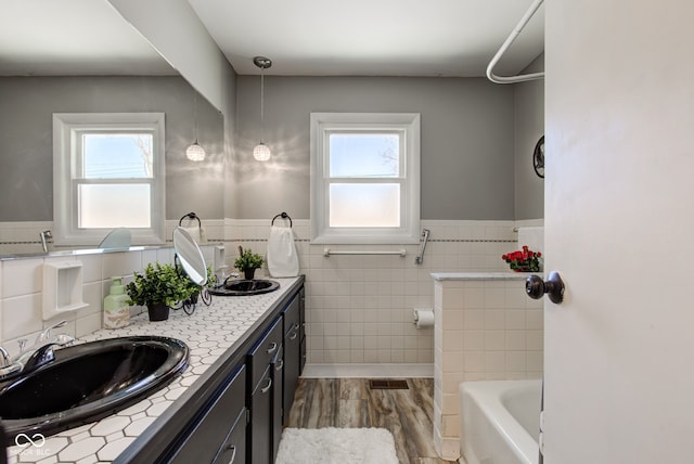 bathroom with a tub to relax in, vanity, wood-type flooring, and tile walls