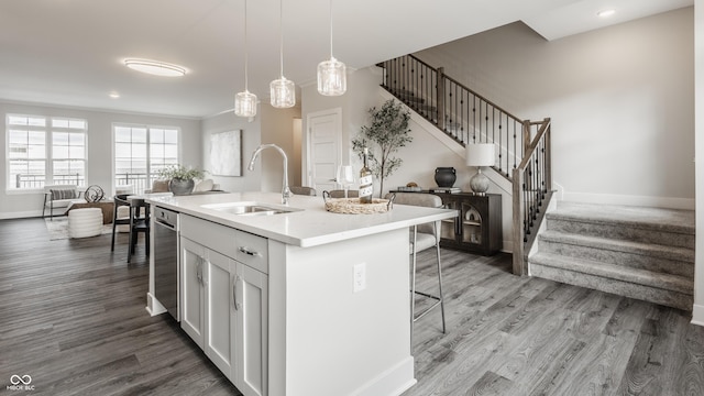 kitchen with a kitchen bar, sink, white cabinets, hanging light fixtures, and an island with sink