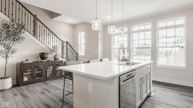 kitchen with sink, stainless steel dishwasher, pendant lighting, a breakfast bar area, and a kitchen island with sink