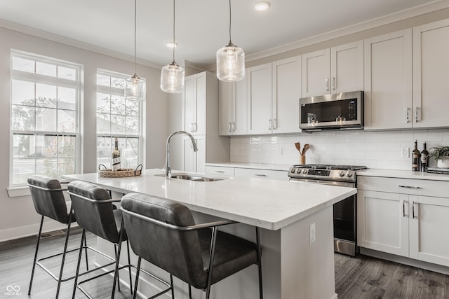 kitchen with light stone counters, stainless steel appliances, sink, decorative light fixtures, and a center island with sink