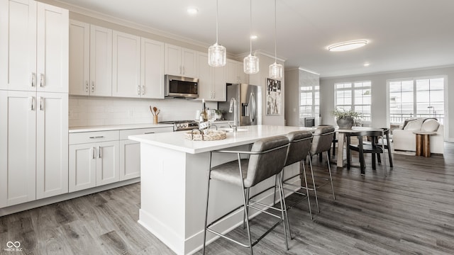 kitchen featuring hanging light fixtures, a center island with sink, white cabinets, and stainless steel appliances