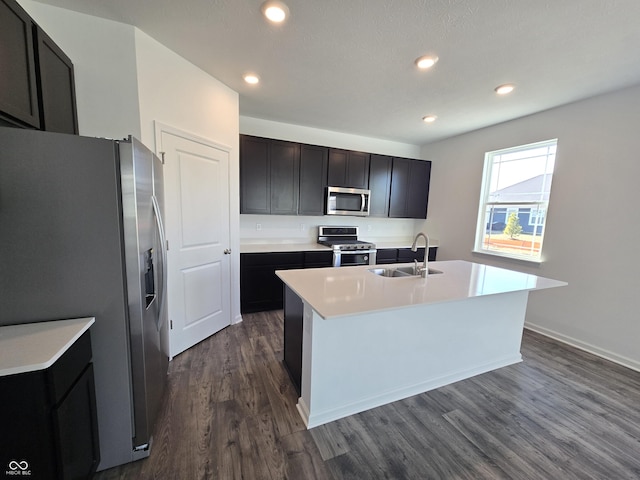 kitchen with dark wood-type flooring, sink, appliances with stainless steel finishes, and an island with sink