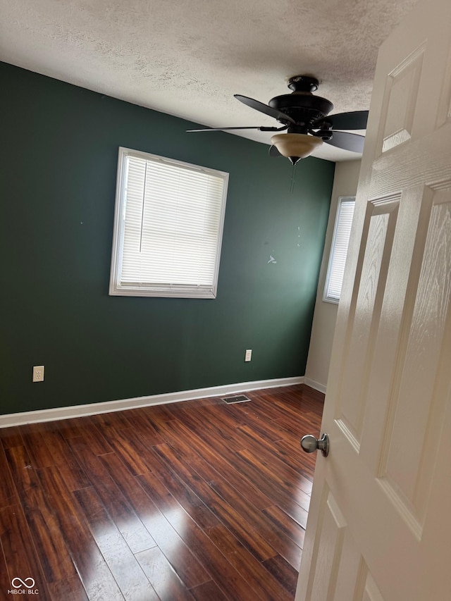 unfurnished room featuring a ceiling fan, a textured ceiling, baseboards, and dark wood-type flooring