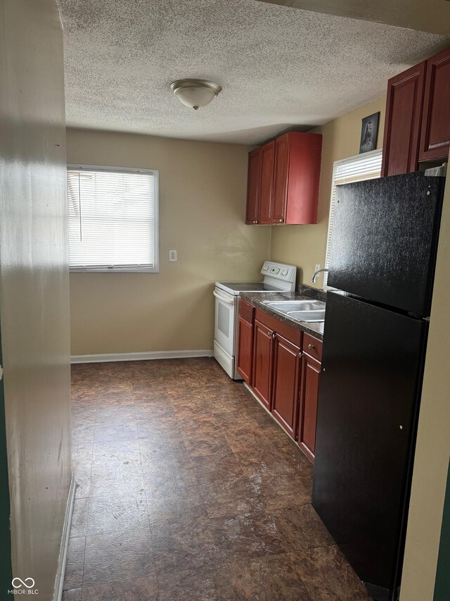 kitchen featuring a sink, baseboards, freestanding refrigerator, dark countertops, and white electric range oven