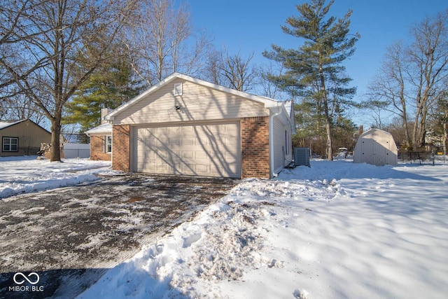 snow covered property featuring a garage, a shed, and central AC unit