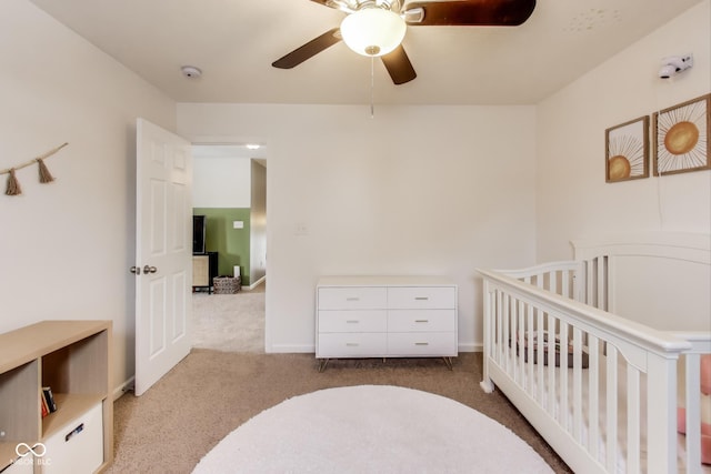 bedroom with a nursery area, light carpet, and ceiling fan