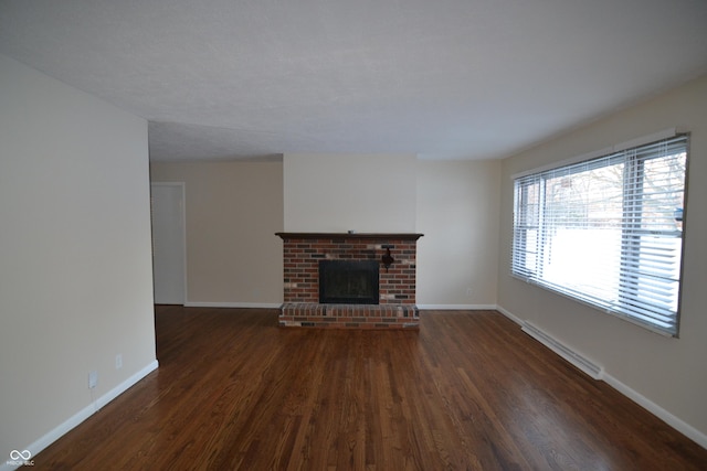 unfurnished living room with a baseboard heating unit, dark hardwood / wood-style flooring, and a brick fireplace