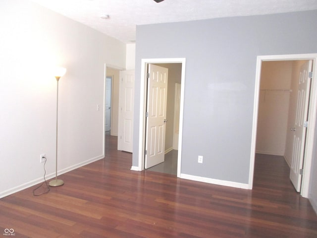 unfurnished bedroom with a spacious closet and dark wood-type flooring