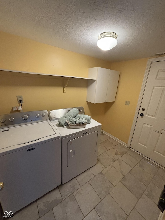 clothes washing area featuring washer and dryer, cabinets, and a textured ceiling