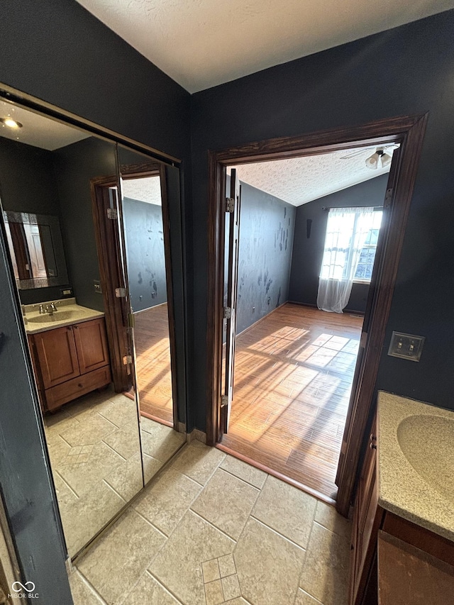 bathroom with a textured ceiling, vanity, and lofted ceiling