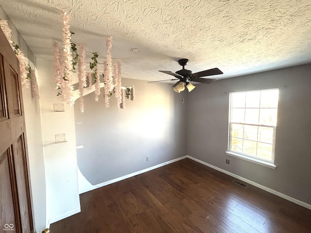 empty room with ceiling fan, dark wood-type flooring, and a textured ceiling