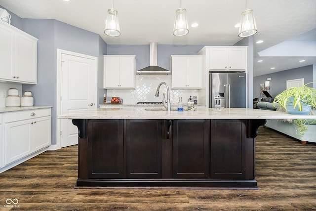 kitchen with high end refrigerator, wall chimney exhaust hood, and a center island with sink