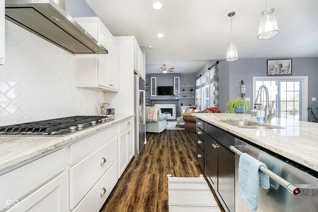 kitchen with sink, appliances with stainless steel finishes, white cabinetry, hanging light fixtures, and wall chimney exhaust hood