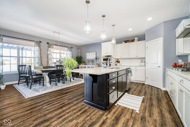 kitchen with sink, dark hardwood / wood-style floors, an island with sink, pendant lighting, and white cabinets