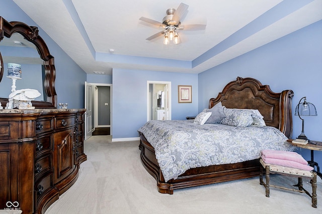 carpeted bedroom with ceiling fan, ensuite bath, and a tray ceiling