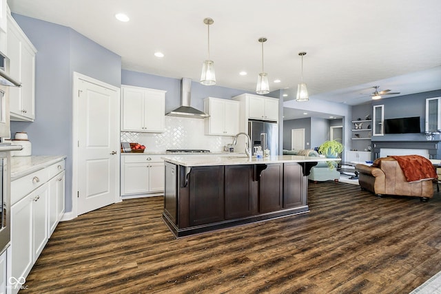 kitchen with pendant lighting, ceiling fan, high end fridge, white cabinetry, and wall chimney exhaust hood